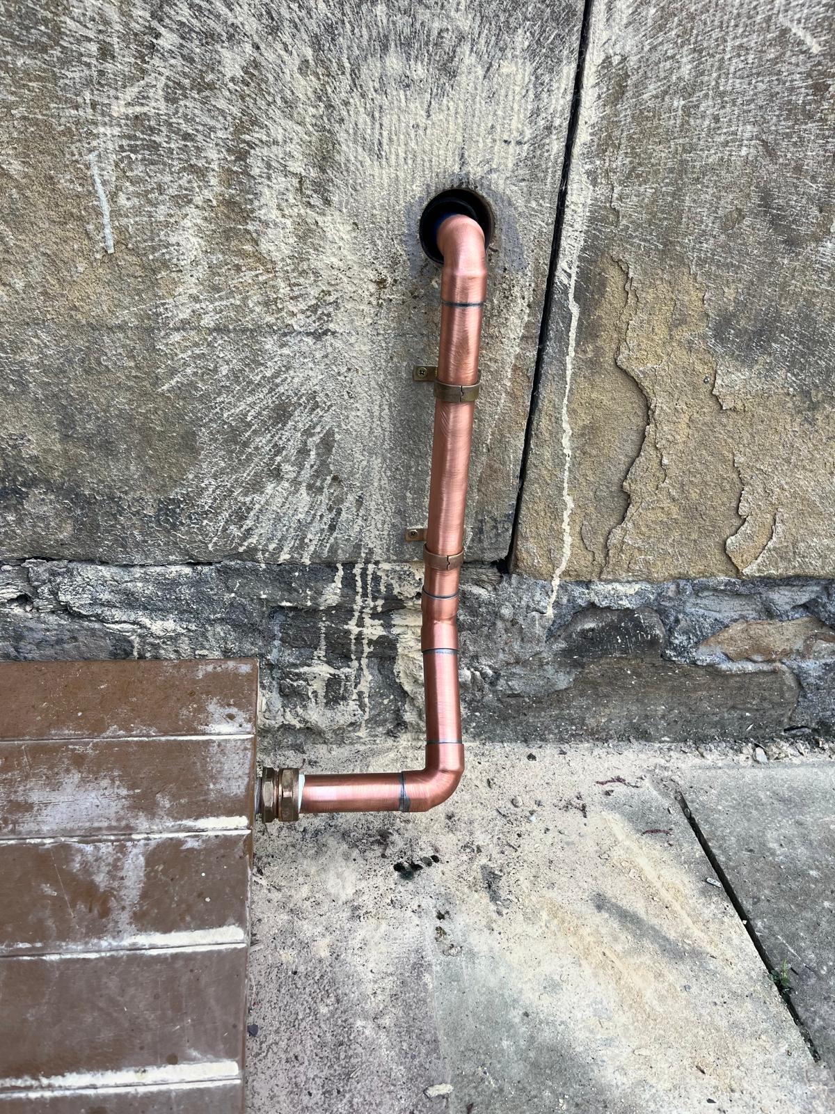 External copper pipework run through a stone wall for a new outside tap installation