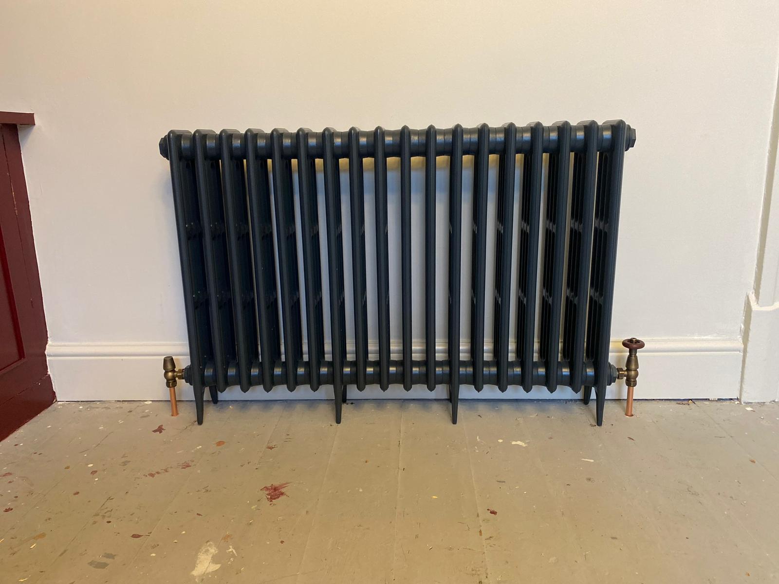 Dark cast iron column radiator installed with antique brass valves and copper pipes